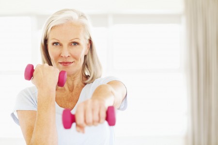 Senior woman lifting dumbbells at gym. Horizontal shot.
